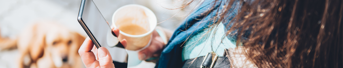 young woman holds an open cup of coffee while looking at her smartphone